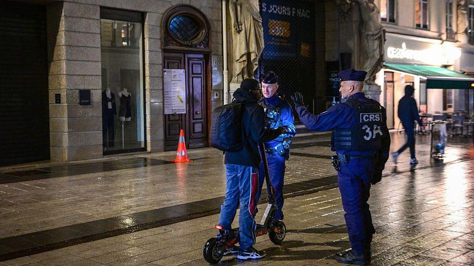 French police officers check a person during a partial curfew in Lyon