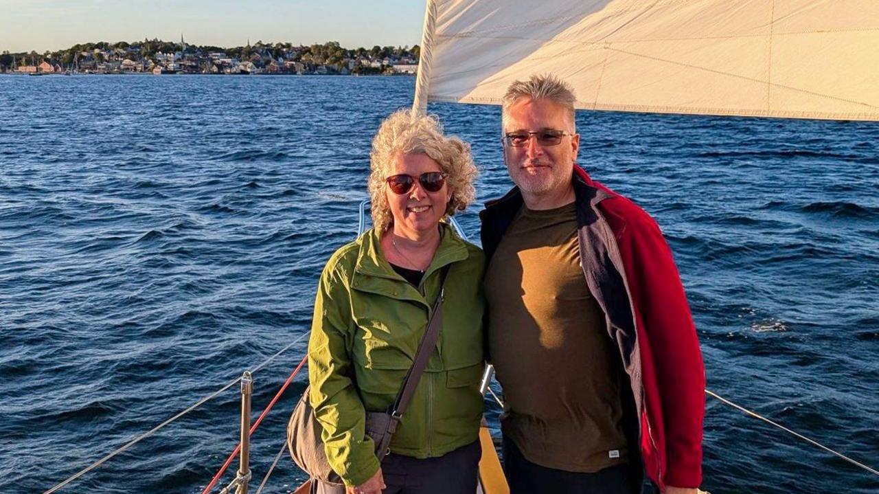 Couple aboard a boat in golden light, standing against blue waters and distant land