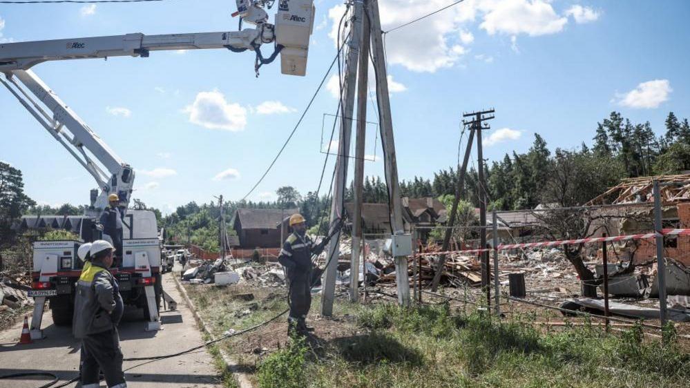 Energy workers stand beneath a power line as they work to restore supply following a strike