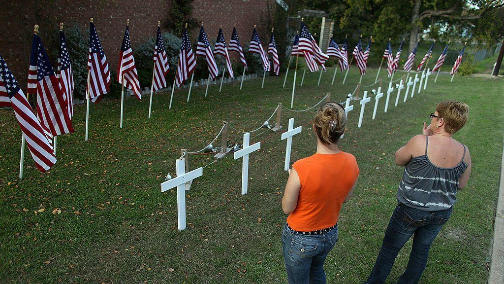 A line of white crosses beside American flags with women staring