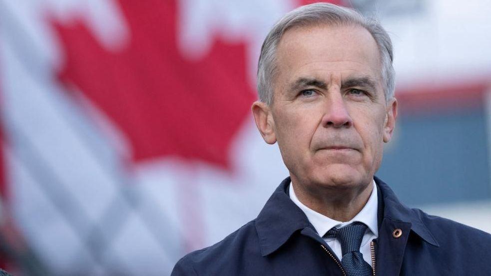 Mark Carney standing with a Canadian flag in the background