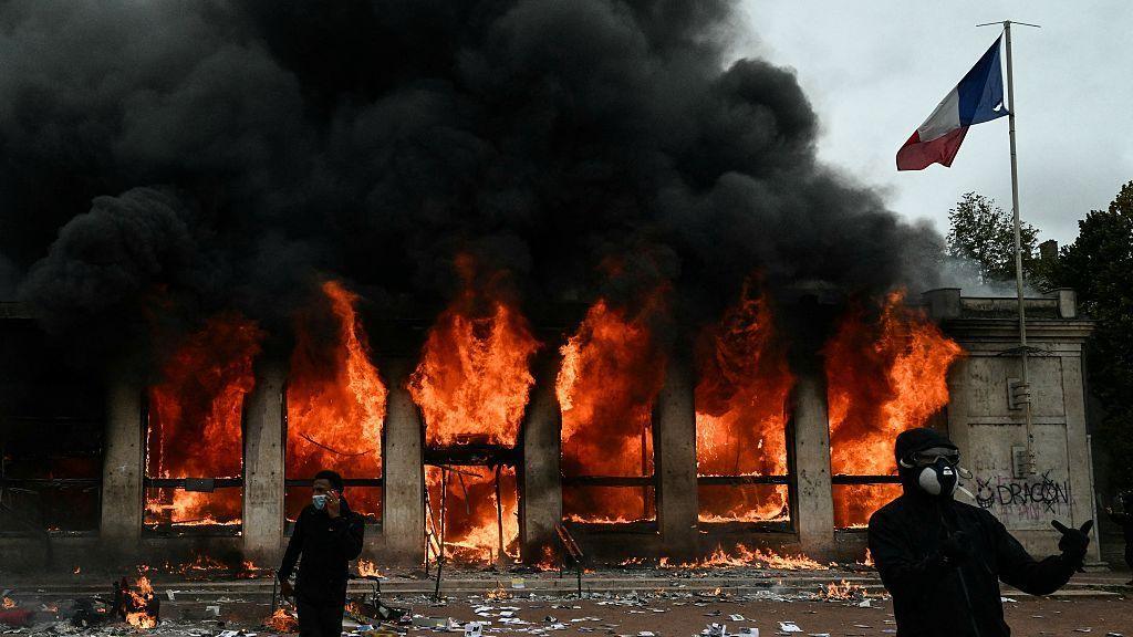 Demonstrators in black and face coverings outside a burning Lyon tourism office
